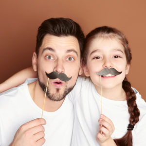A father and daughter smiling and holding false mustaches to their faces | the penny pack