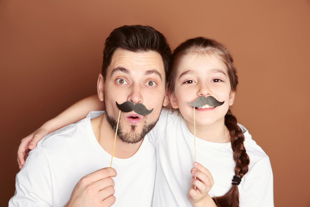 A father and daughter smiling and holding false mustaches to their faces | the penny pack